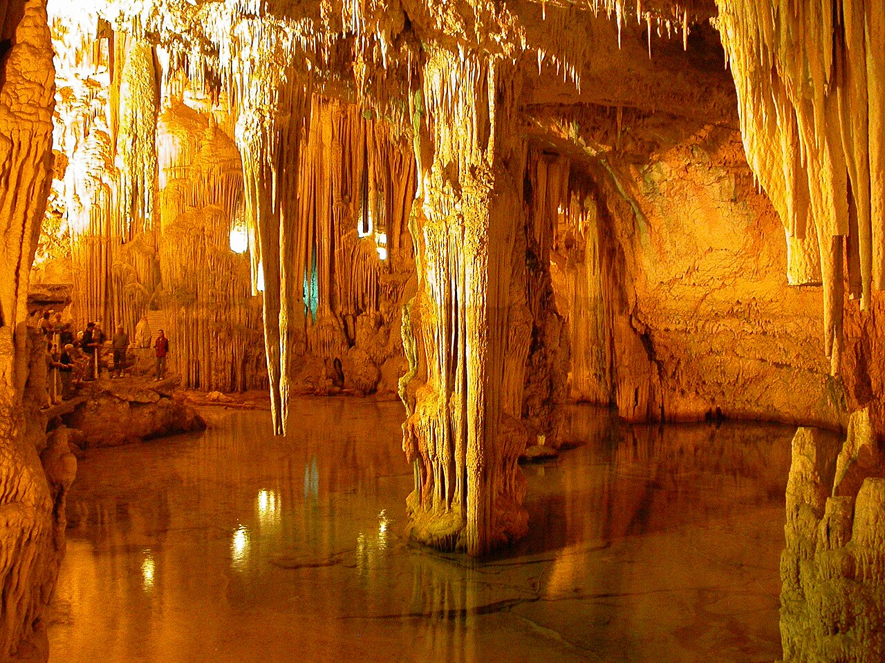 Wnętrze Groty Neptuna: stalaktyty i stalagmity nad podziemnym jeziorem.